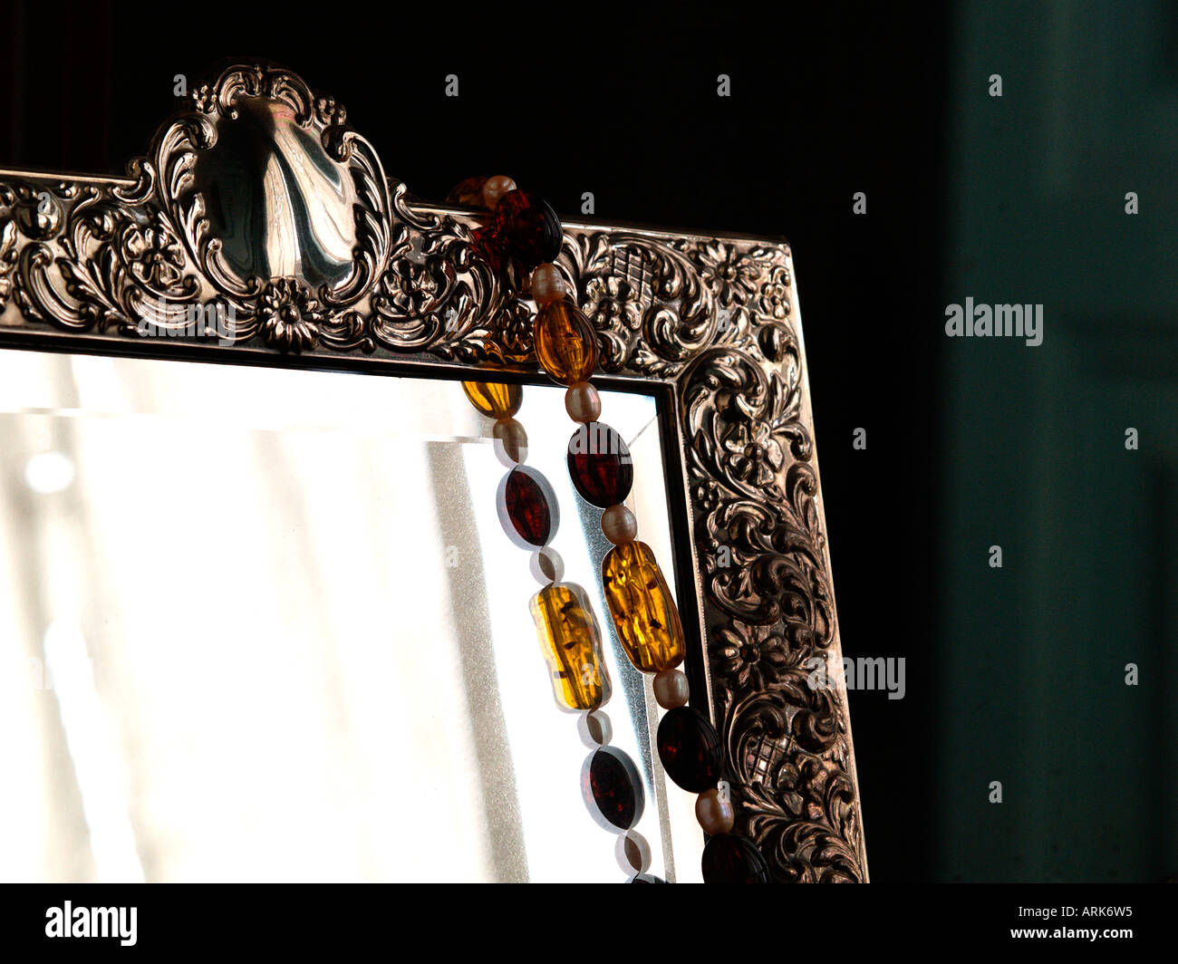 corner of mirror with ornate silver frame and amber necklace Stock Photo