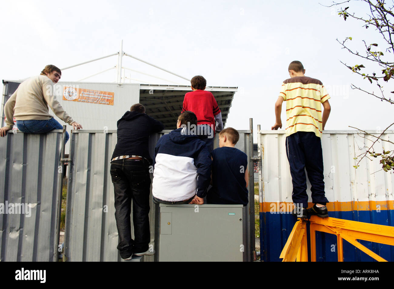Group of young boys climb on a fence to watch a football game for free Stock Photo