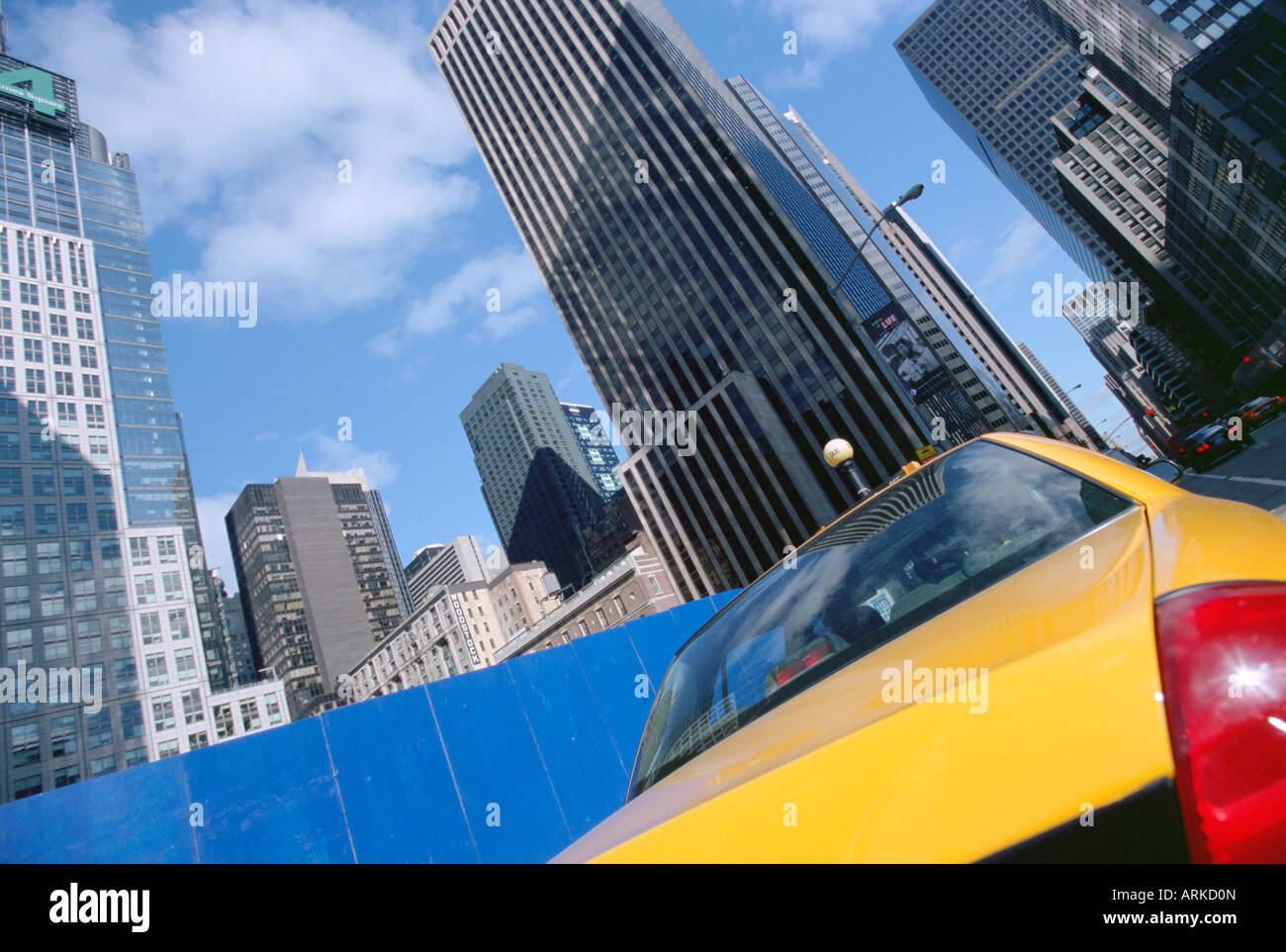 Yellow taxi cab passing blue board with skyscrapers beyond, New York City, New York, USA, North America Stock Photo
