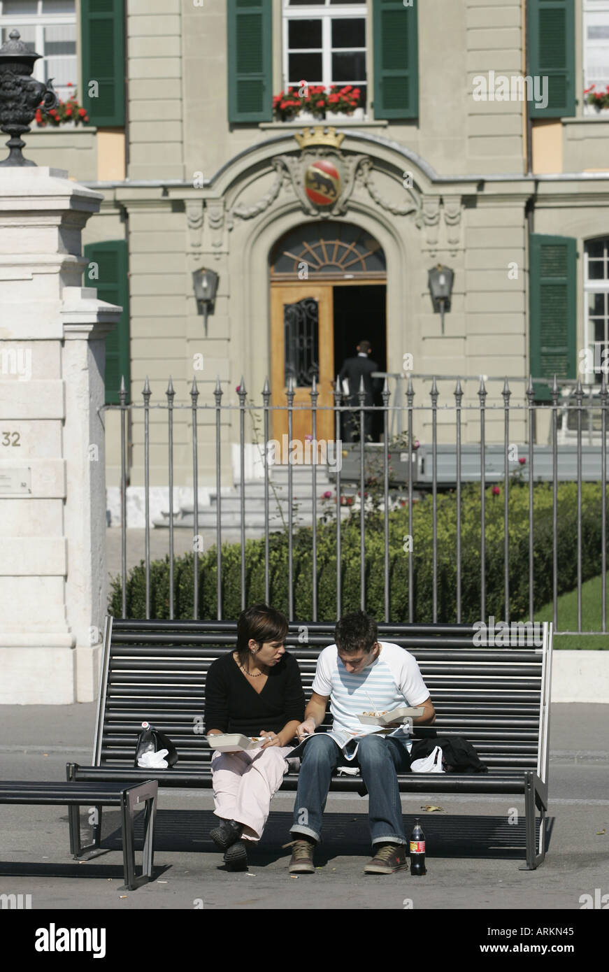 Young couple sitting on a bench eating fast food in front of the former old boys orphanage in Berne, Switzerland. Stock Photo
