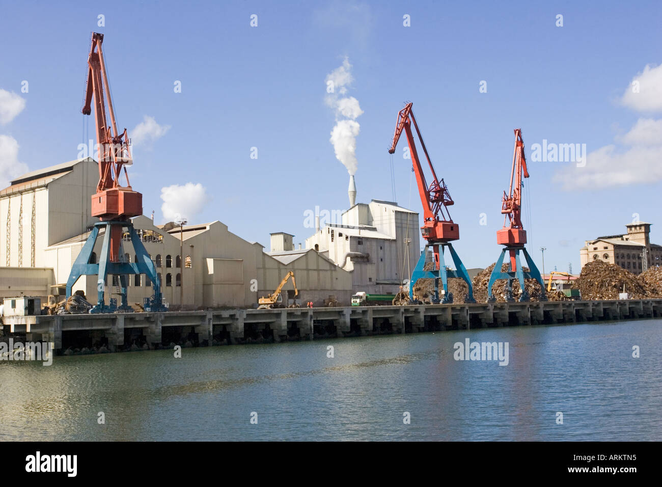 Cranes on quayside unloading scrap metal into trucks for reprocessing ...