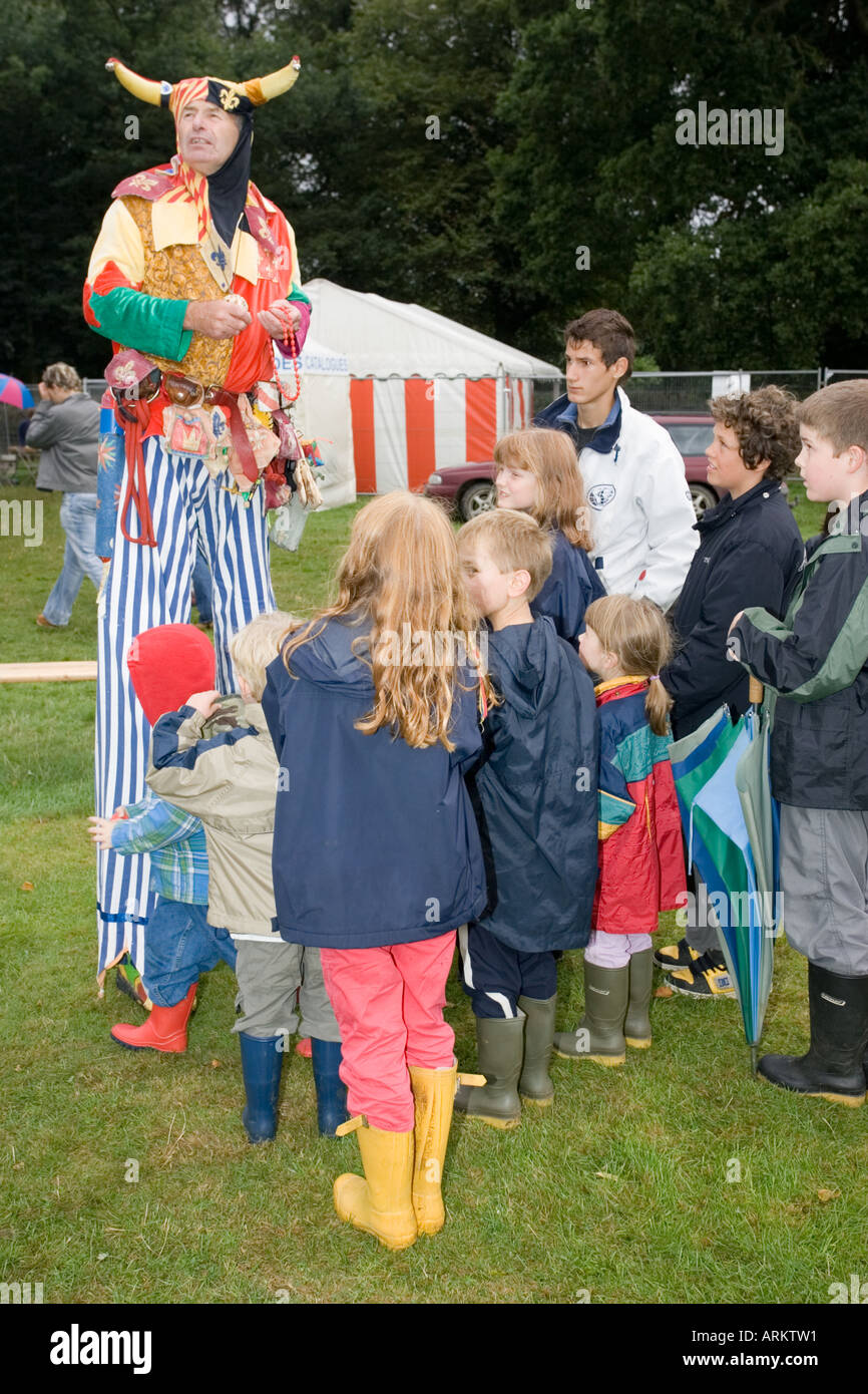 Tall colourful clown on stilts wearing hat with horns entertaining