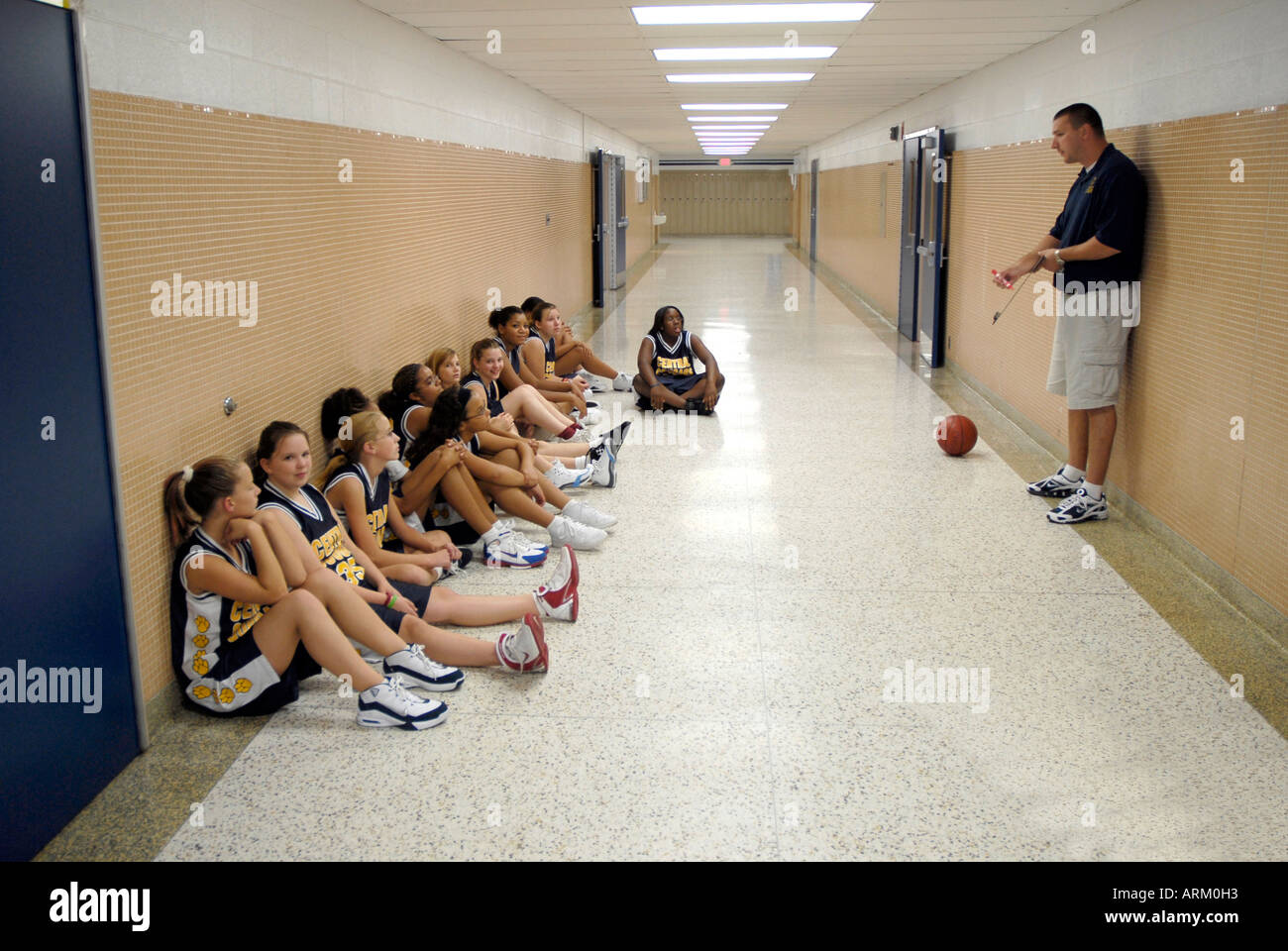Coach talks with his 8th grade girls basketball team in the school hallway during halftime of a basketball game Stock Photo