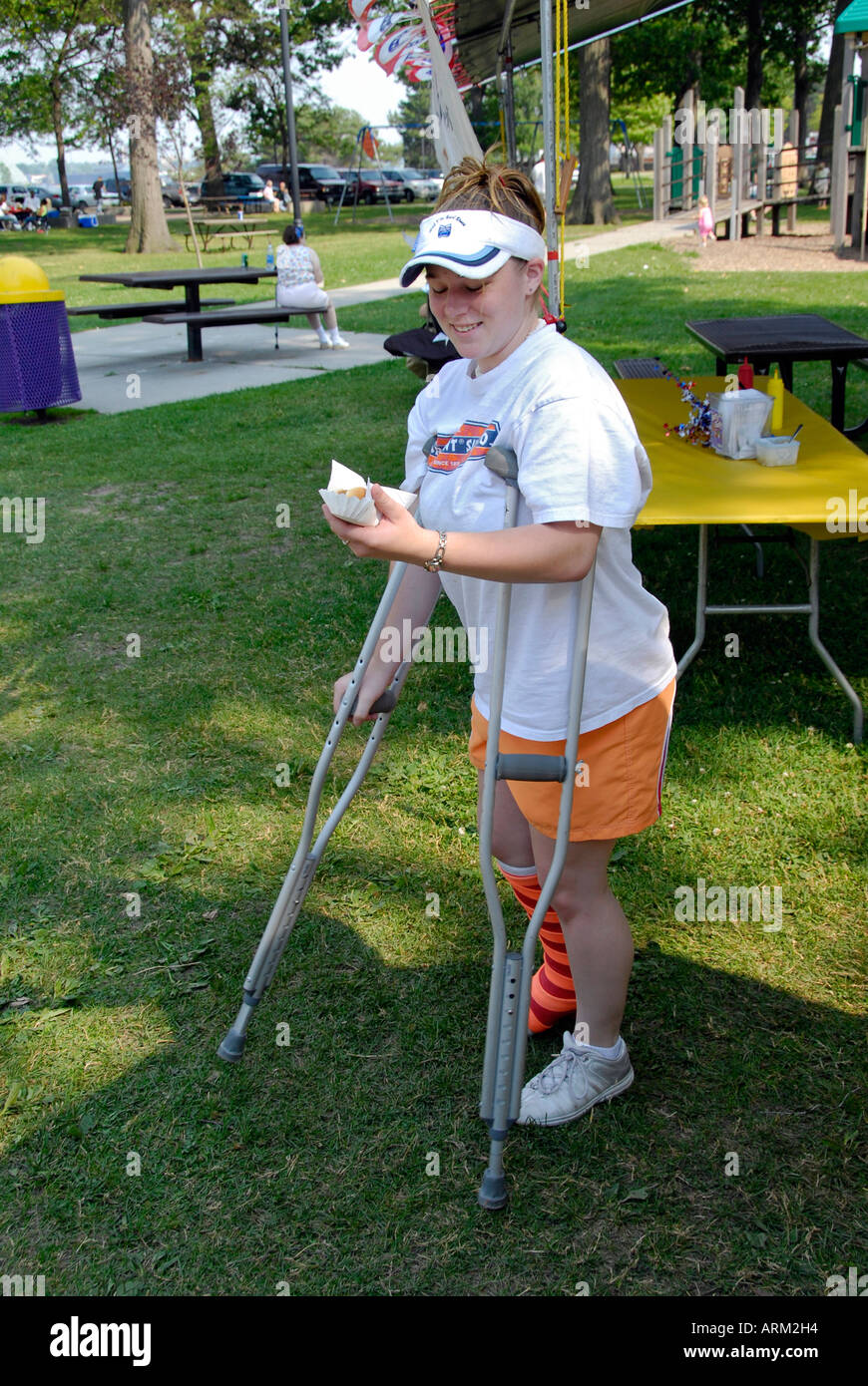 Injured girl walking on crutches with a hot dog in her hand Stock Photo