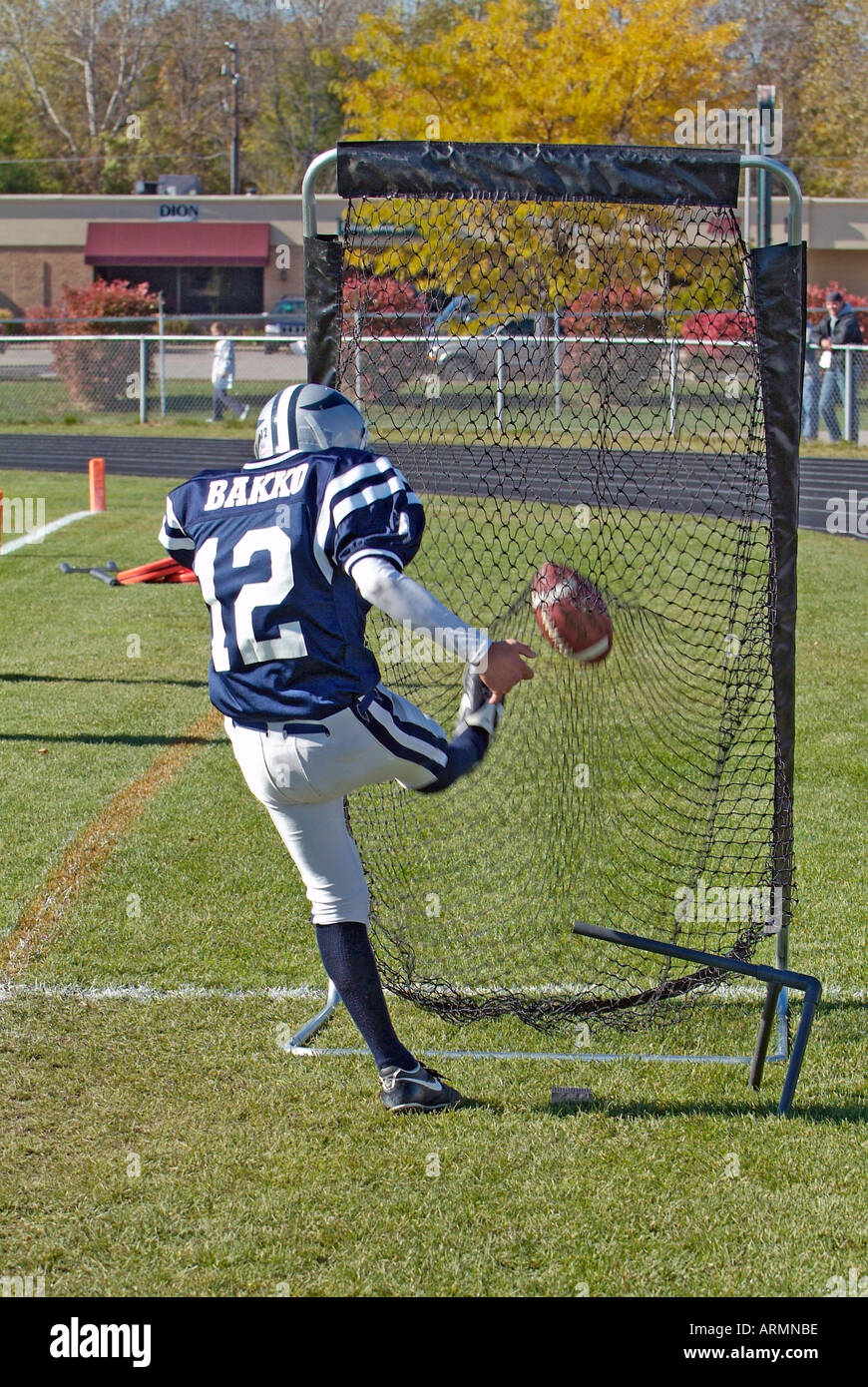Football player practices kicking football into a net prior to