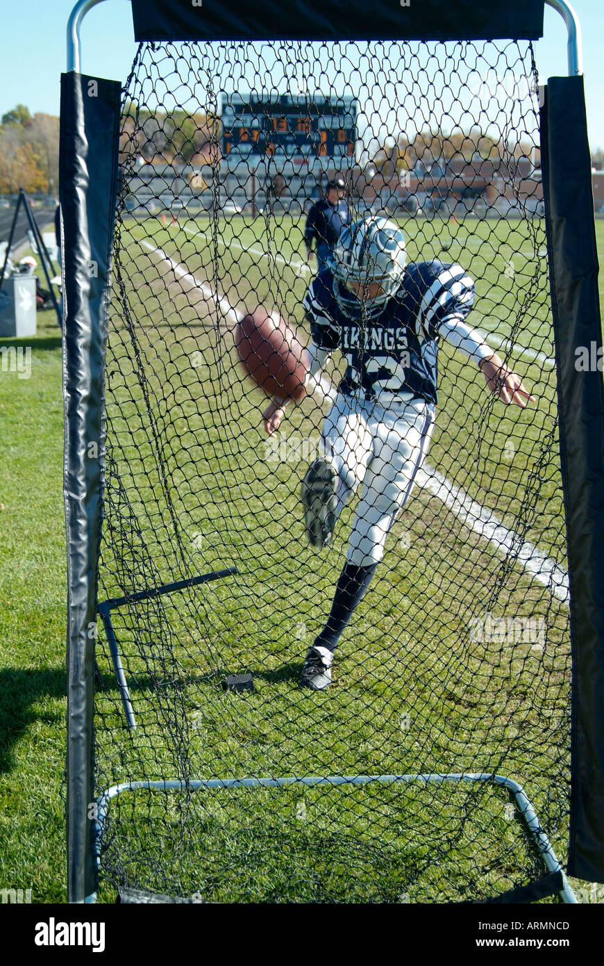 Football player practices kicking football into a net prior to