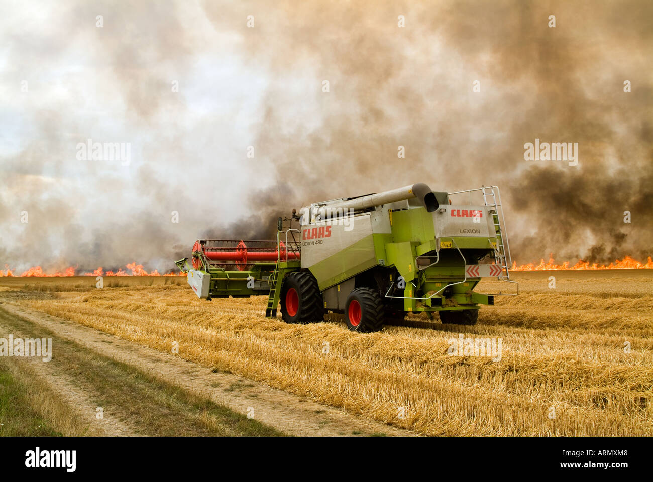 A combine harvester in the middle ground racing towards a field fire to