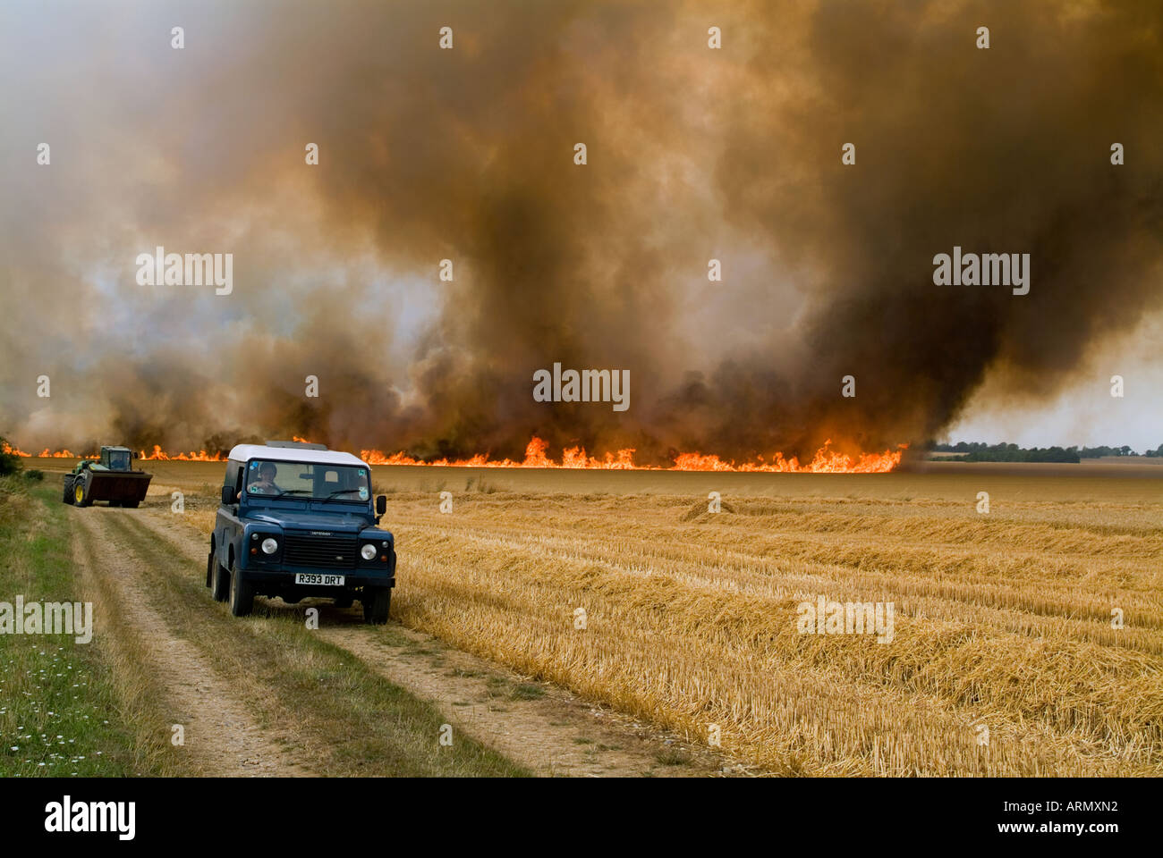A Landrover racing away from a field fire with smoke and flames in the