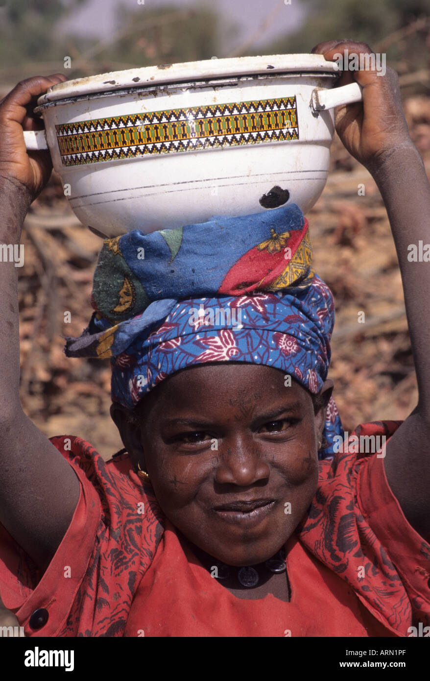 Kankamtuti, Niger, Africa. Fulani Girl with Facial Scarification Carrying Bowl of Food on Head. Stock Photo