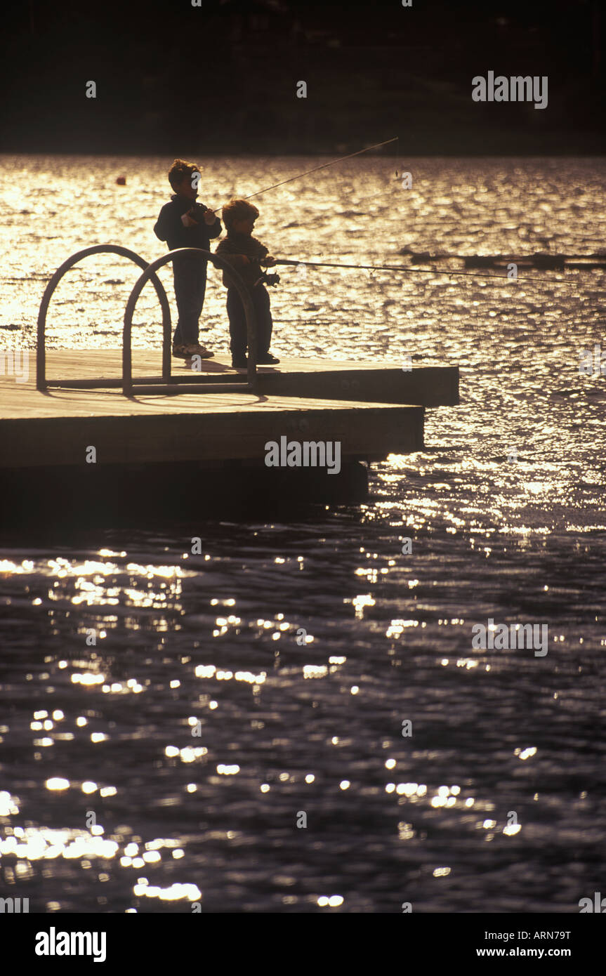 Two boys fish from floating dock by lakeside, British Columbia, Canada. Stock Photo