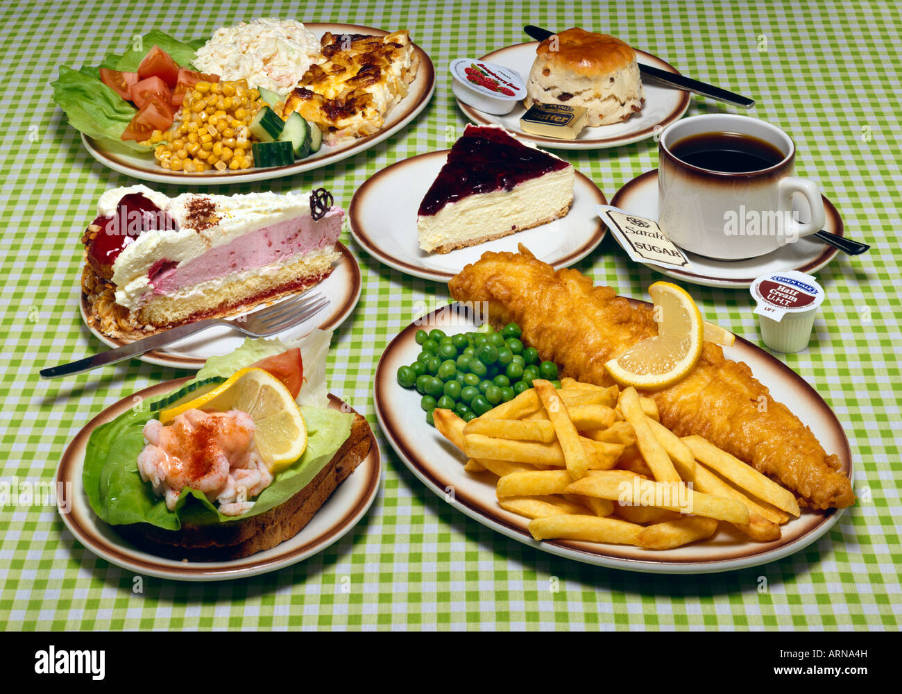 Selection Of Food  including fish & chips, salads, deserts coffee & a scone on a green gingham cloth on a Dinning table Stock Photo