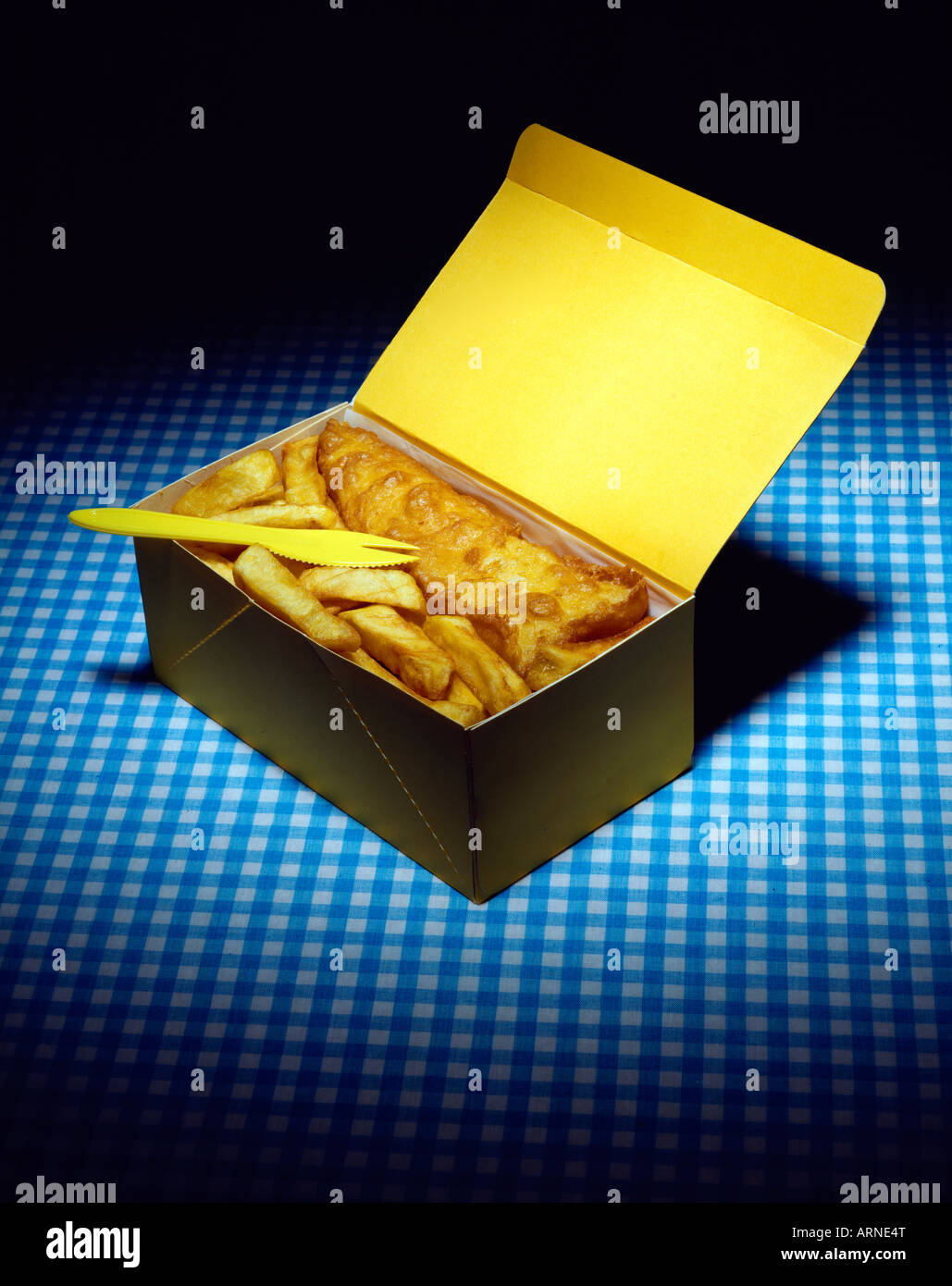 Traditional British Fish & Chips spotlit, presented in a cardboard take out box with a plastic fork on a blue gingham tablecloth Stock Photo