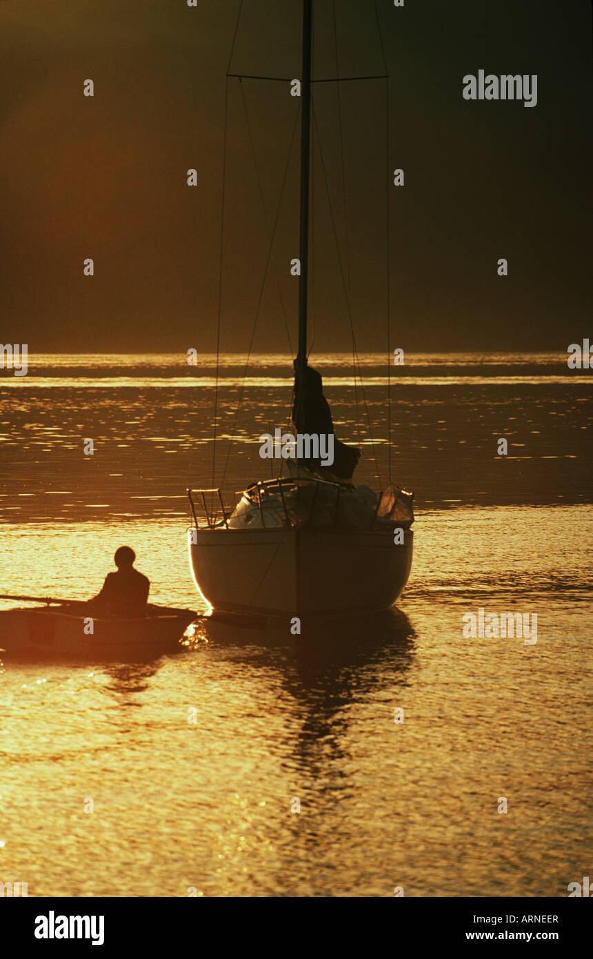 sailor approaches boat in dinghy, sunset, Vancouver Island, British Columbia, Canada. Stock Photo