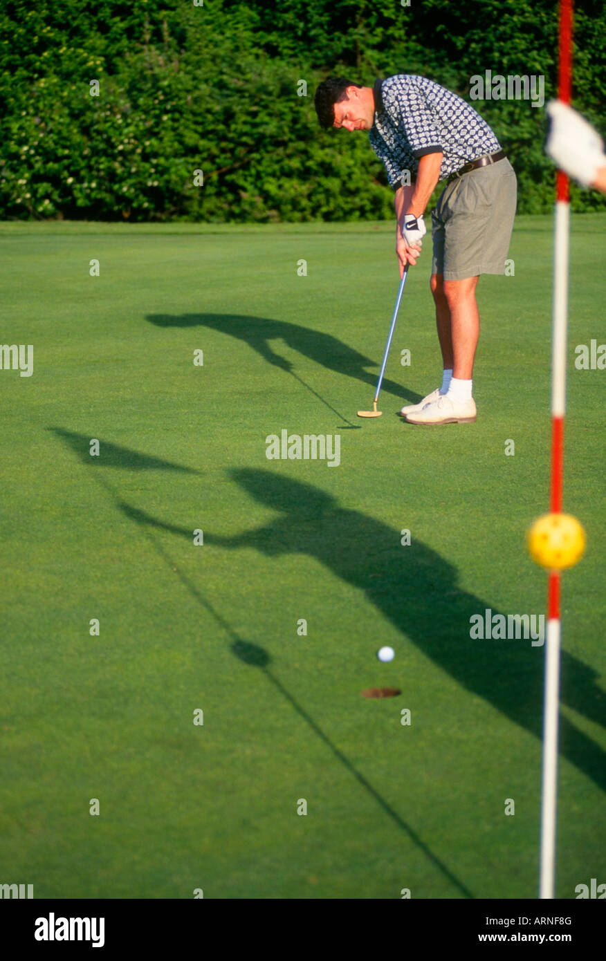 athletic 20 something golfer putts ball, shadow of partner on grass, Victoria, Vancouver Island, British Columbia, Canada. Stock Photo