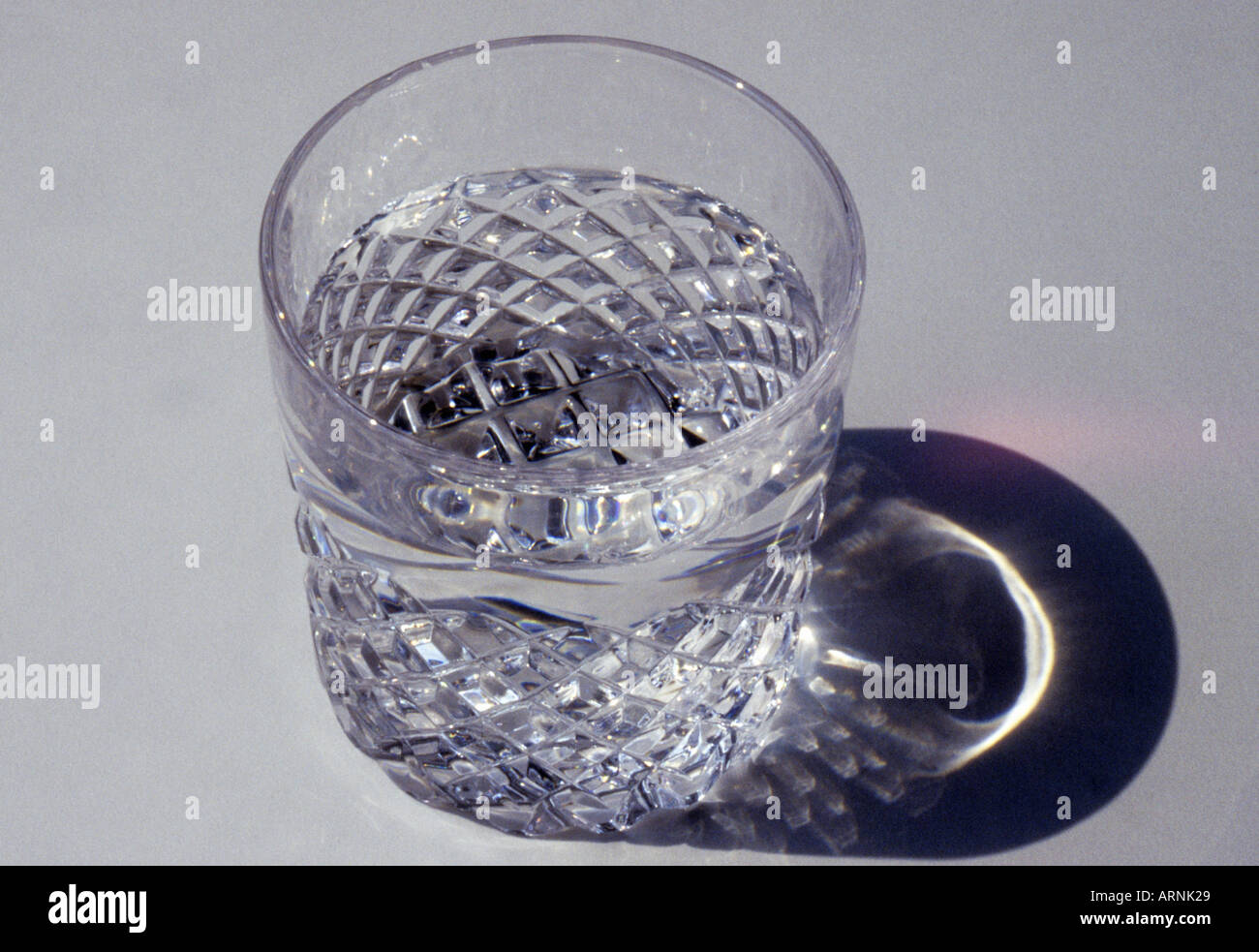 Crystal glass of water on a white table casting a shadow. Nobody Stock Photo