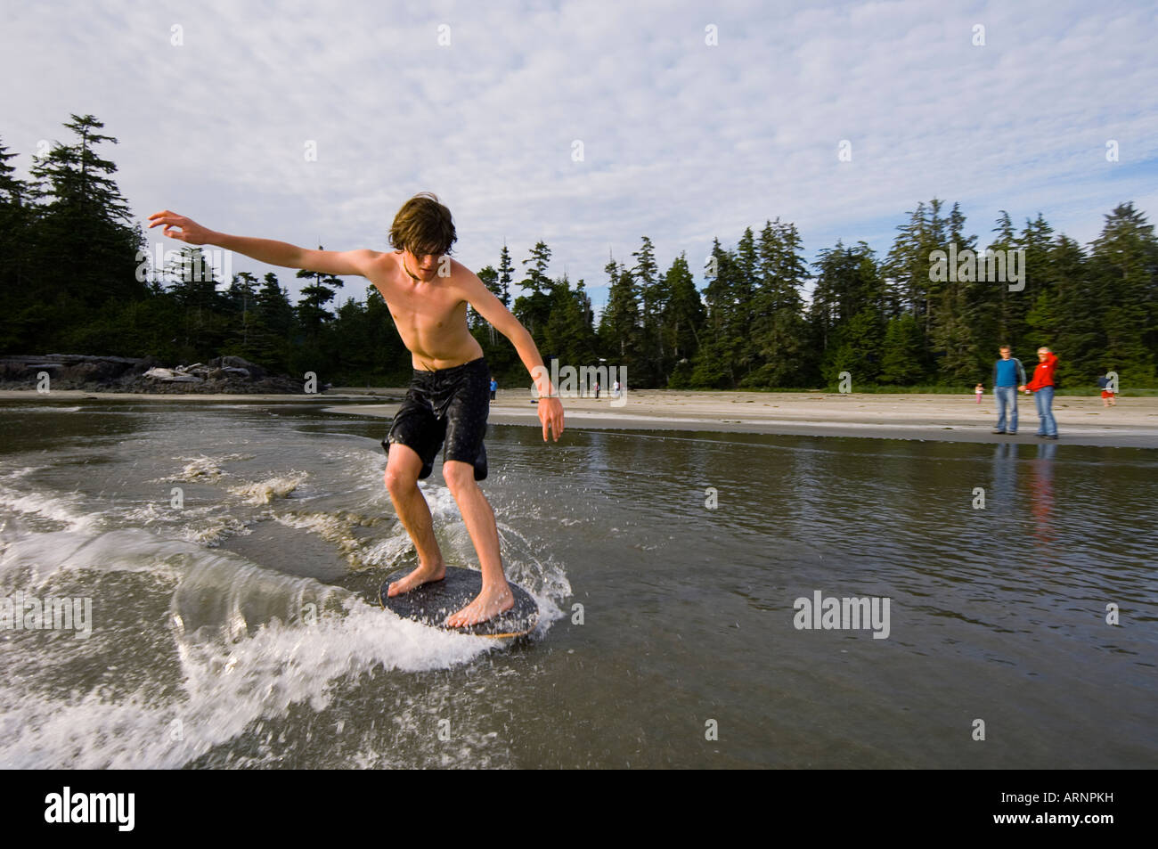 teenage boy skim boards on wet sand, MacKenzie Beach at Tofino