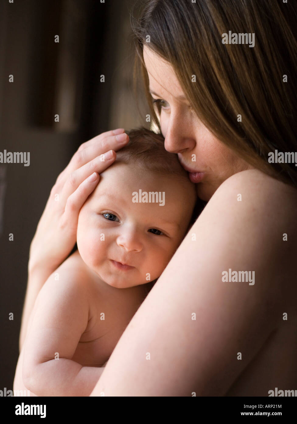 portrait of mother holding two month old baby boy skin to skin, hand on head, window light, hugging, holding Stock Photo