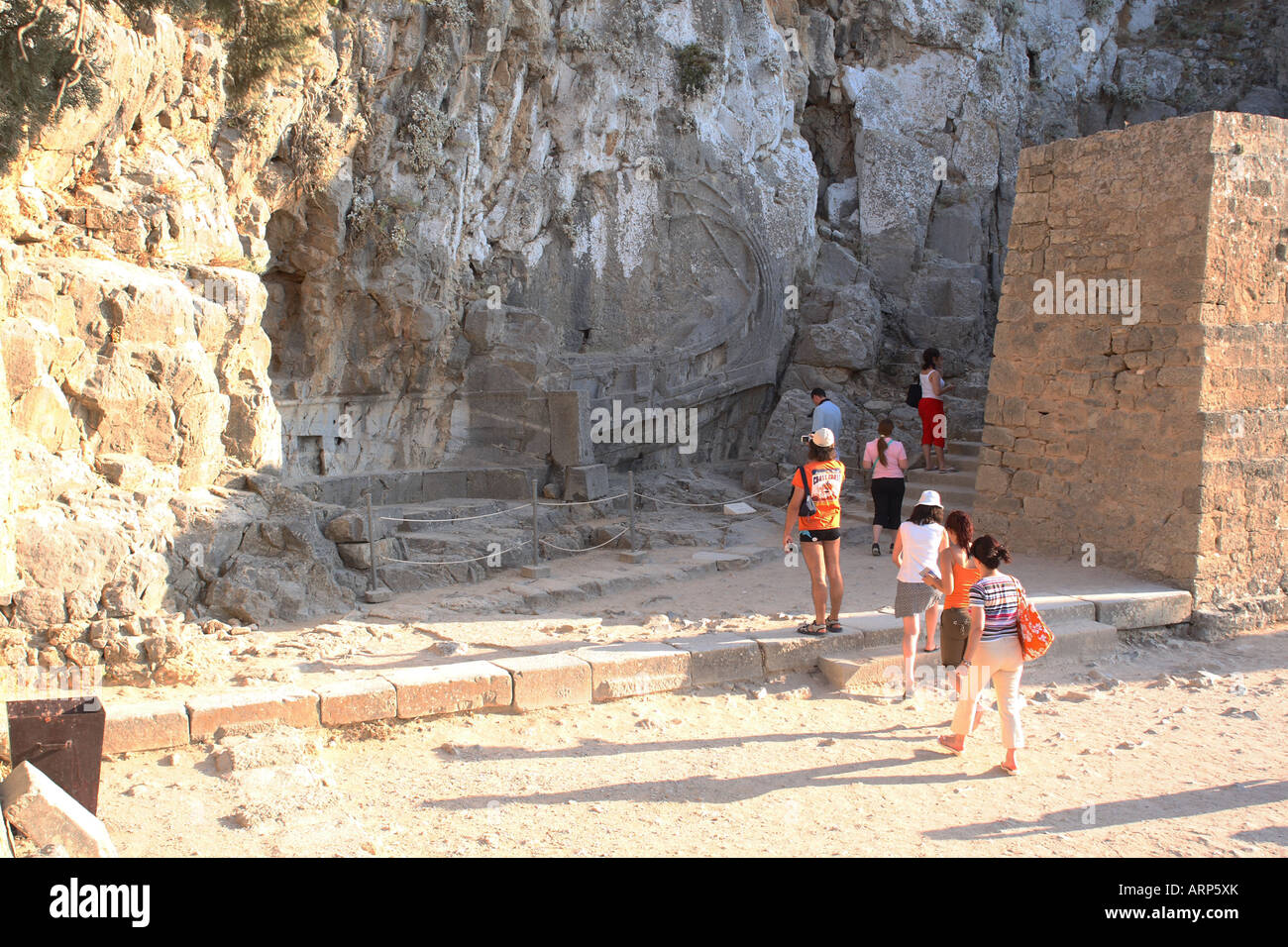 Tourist pass the ship carved out of the rock face at the accent of The Acropolis Lindos Rhodes Island Greece Stock Photo
