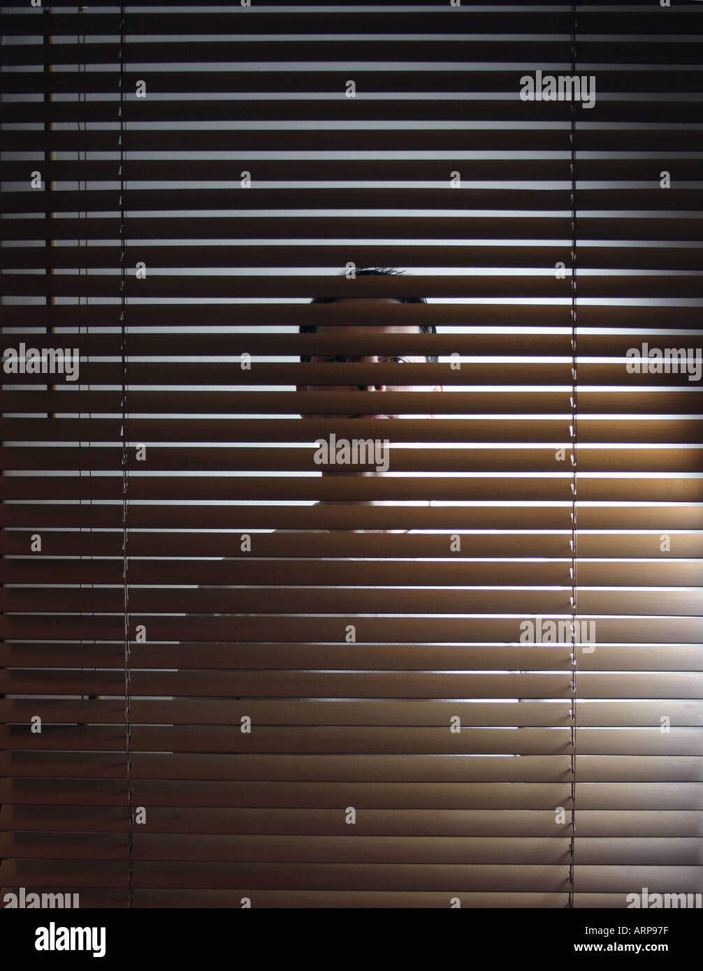 Man behind venetian blinds peeking Stock Photo