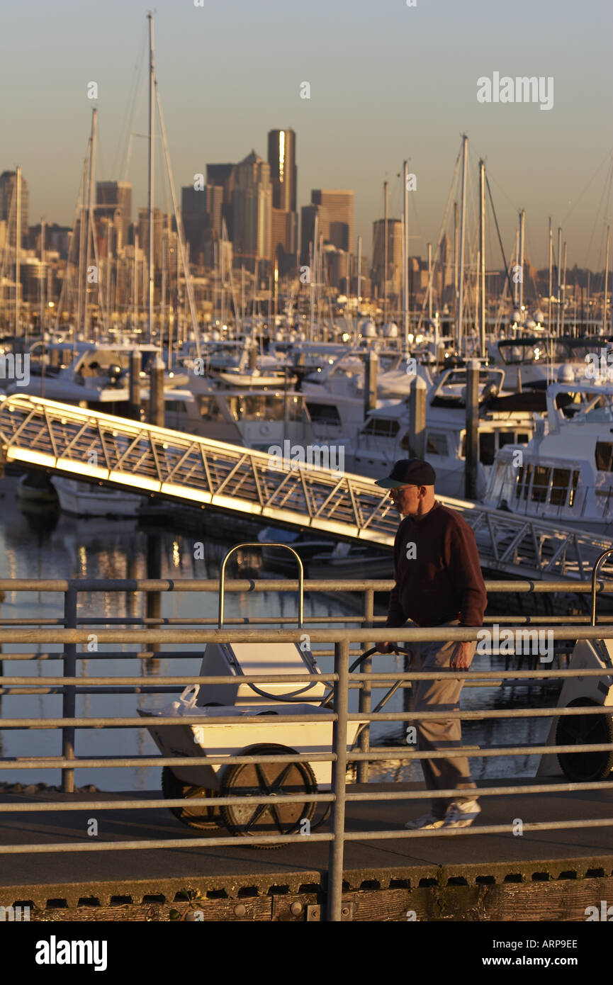 Man with cart on ramp at boat marina with Seattle Washington skyline in background Stock Photo