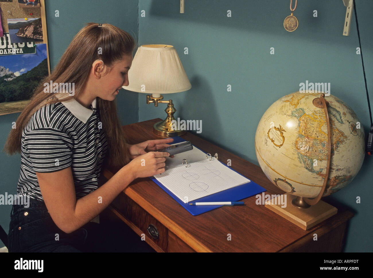 Teen doing math homework in bedroom at desk, hearing aid, Ohio USA Stock Photo