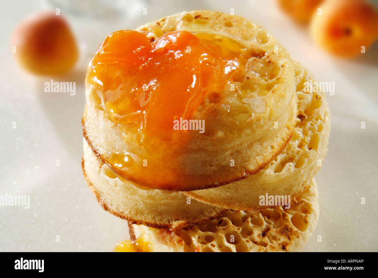 Close up of buttered toasted crumpets with apricot jam ready to eat in a white table setting Stock Photo