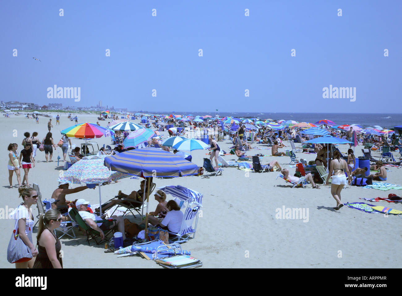 Crowd of people with colorful beach umbrellas, chairs and towels relaxing on sandy beach at New Jersey shore. Stock Photo