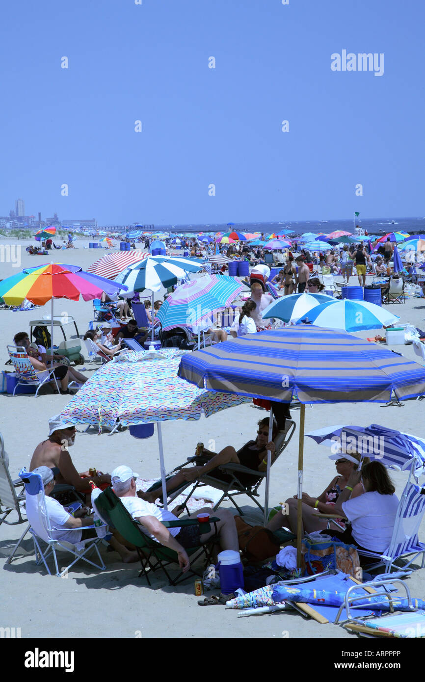 Group of people sitting on lawn chairs under three overlapping beach umbrellas on sandy beach Stock Photo