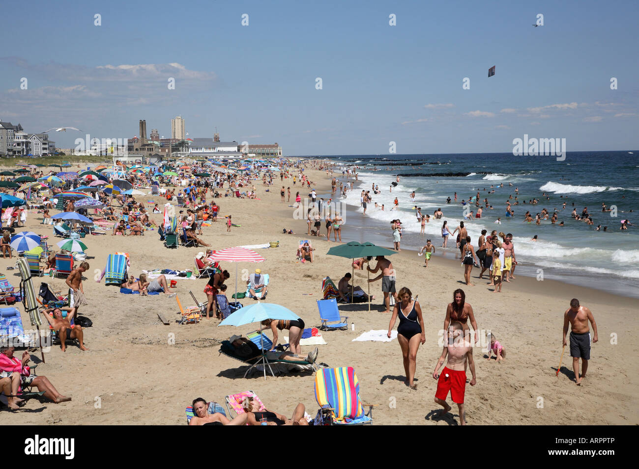 Surfline of a jersey shore beach with mass of people intermixed with colorful umbrellas and banner flyer. Stock Photo