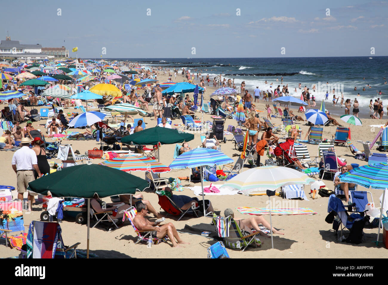 Mass of people with colorful beach umbrellas, chairs, towels and other paraphernalia clustered together all along sandy shore Stock Photo