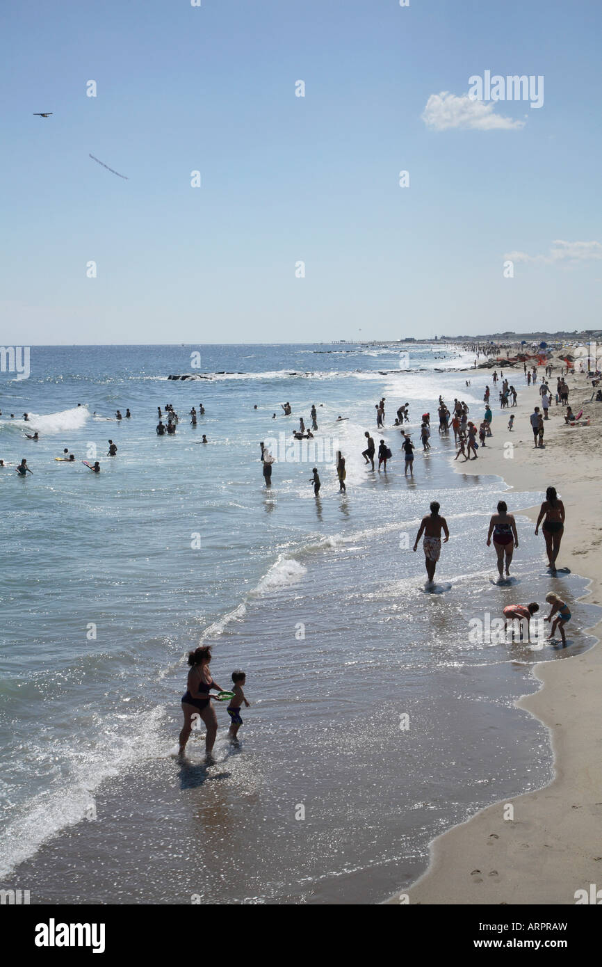 Shoreline of sandy beach from above with people walking along in very shallow water of recently broken and retreating wave. Stock Photo