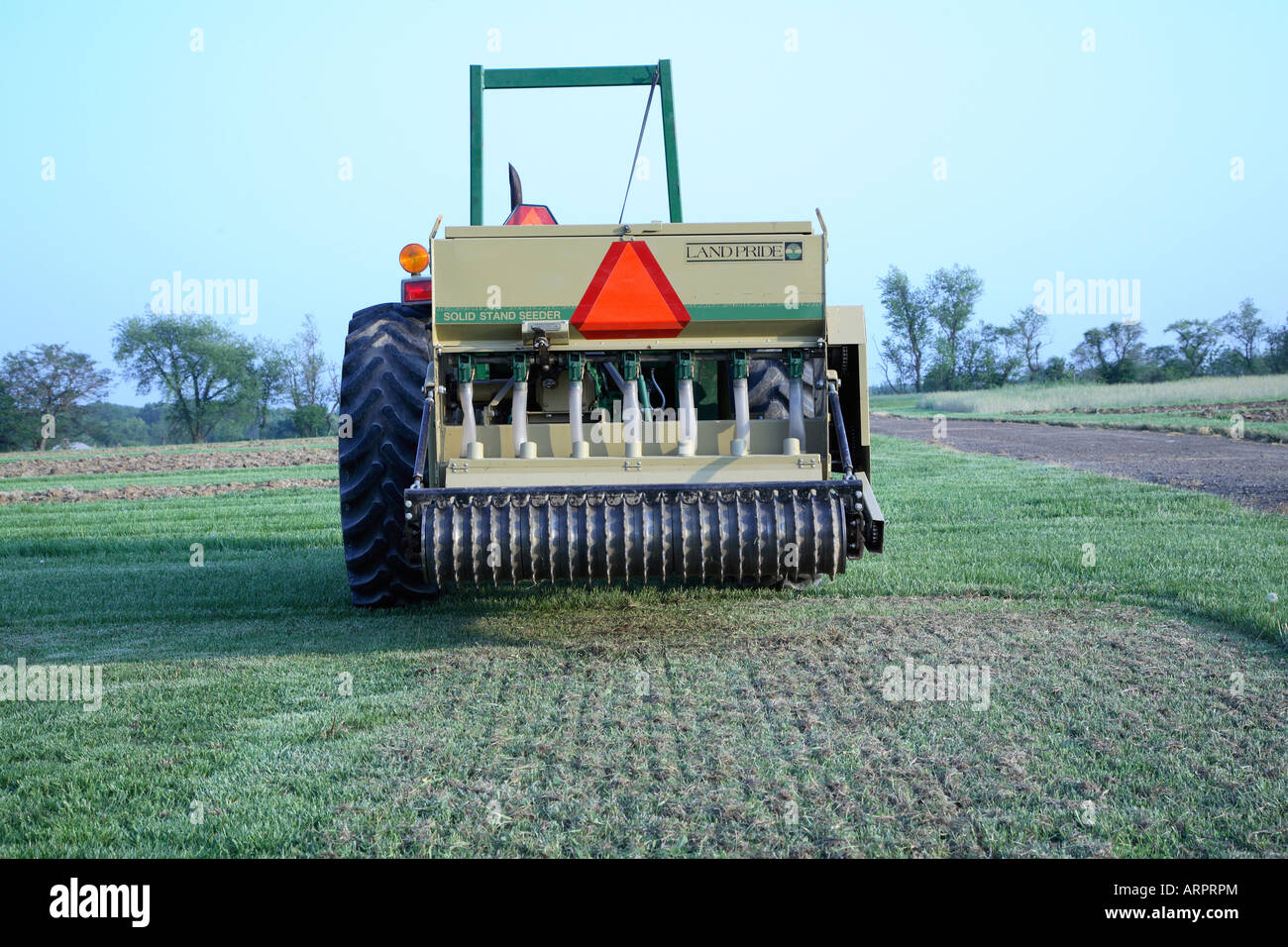 Seeder behind a small tractor ridged metal rollers have cut slits in the existing turf to plant the new seed. Stock Photo