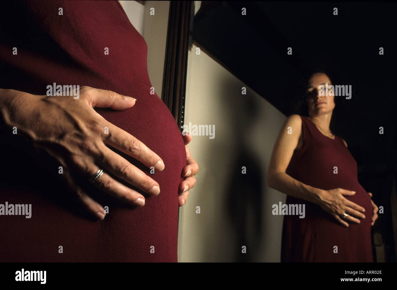 Pregnant woman looking at herself in a mirror and contemplating her future child. Stock Photo