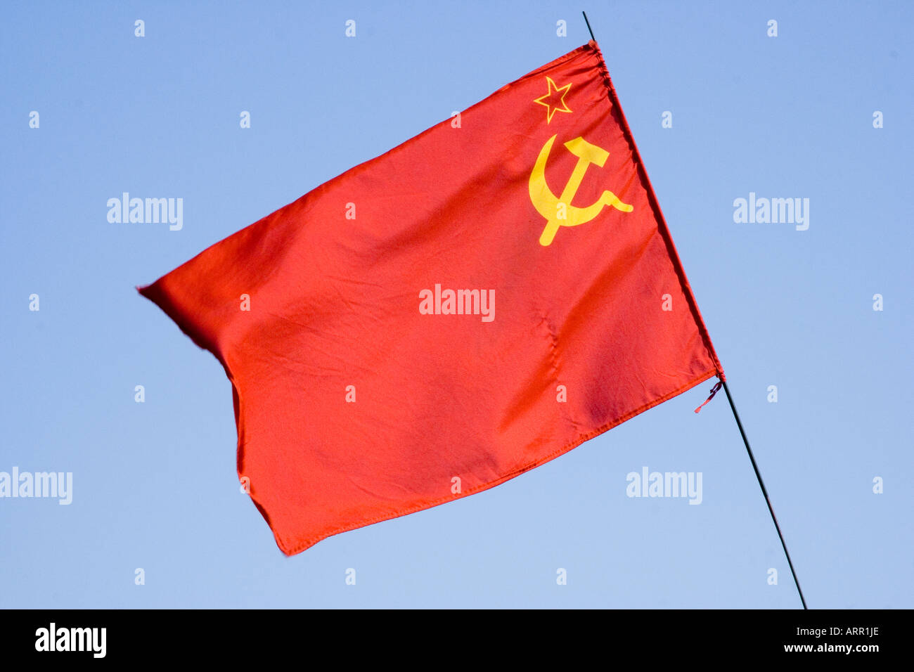 Russian Communist flag, red flag with the hammer and sickle and outline of star in yellow, fluttering against blue sky. Stock Photo