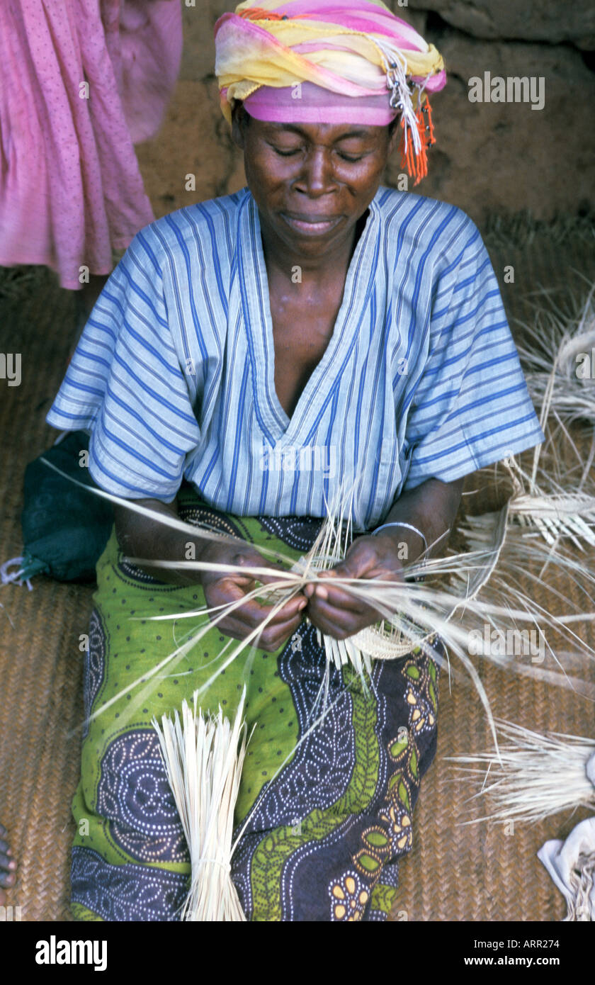AFRICA KENYA KWALI Kenyan woman dressed in traditional kanga cloth weaving a straw mat on the porch of her rural home Stock Photo