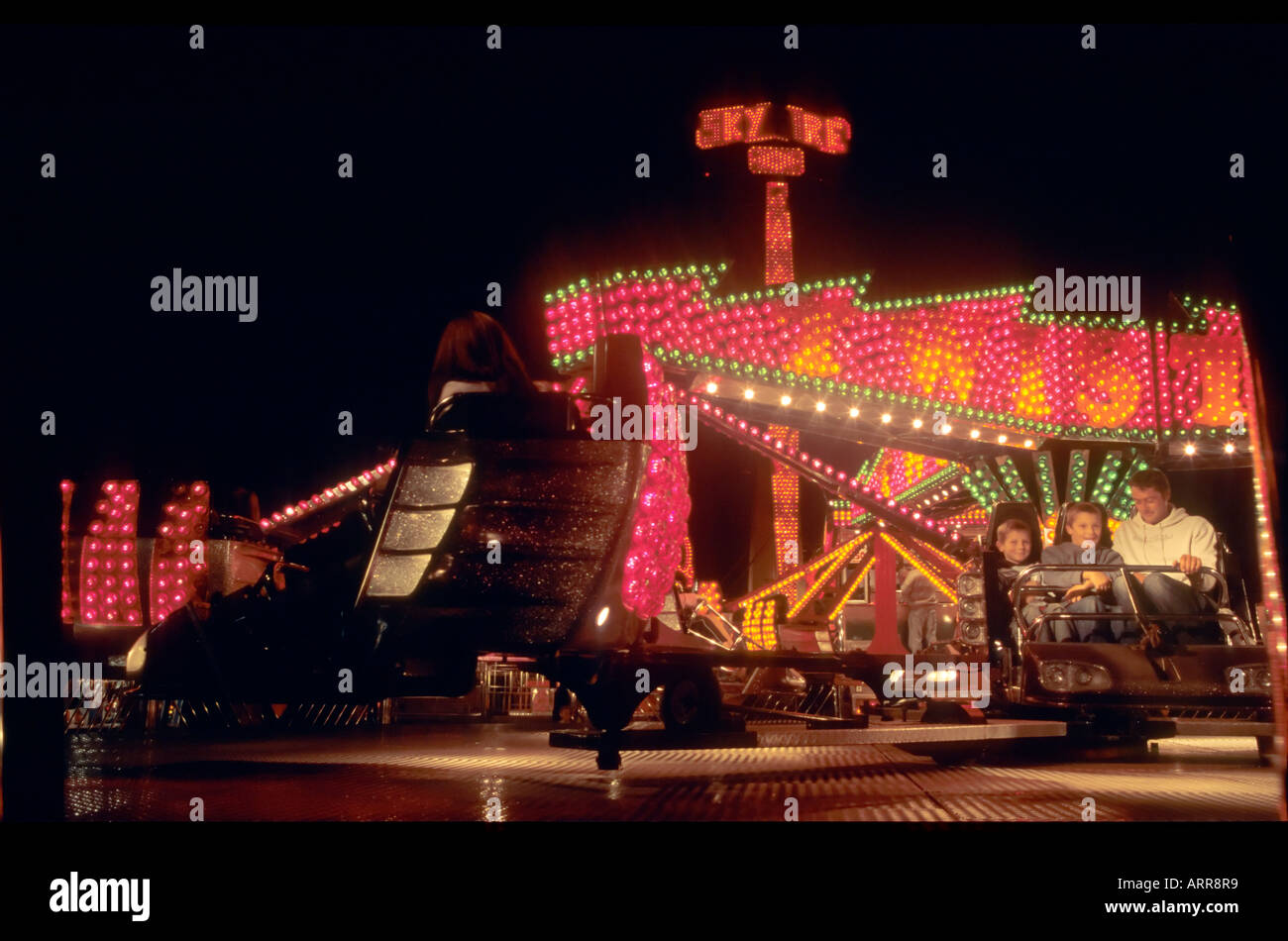 A man and two boys sitting in a fairground ride at night Stock Photo