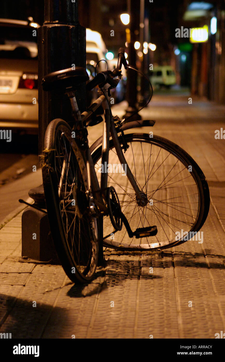 abandoned old walk bicycle tied with padlock and chain to a beacon in the street at night Stock Photo