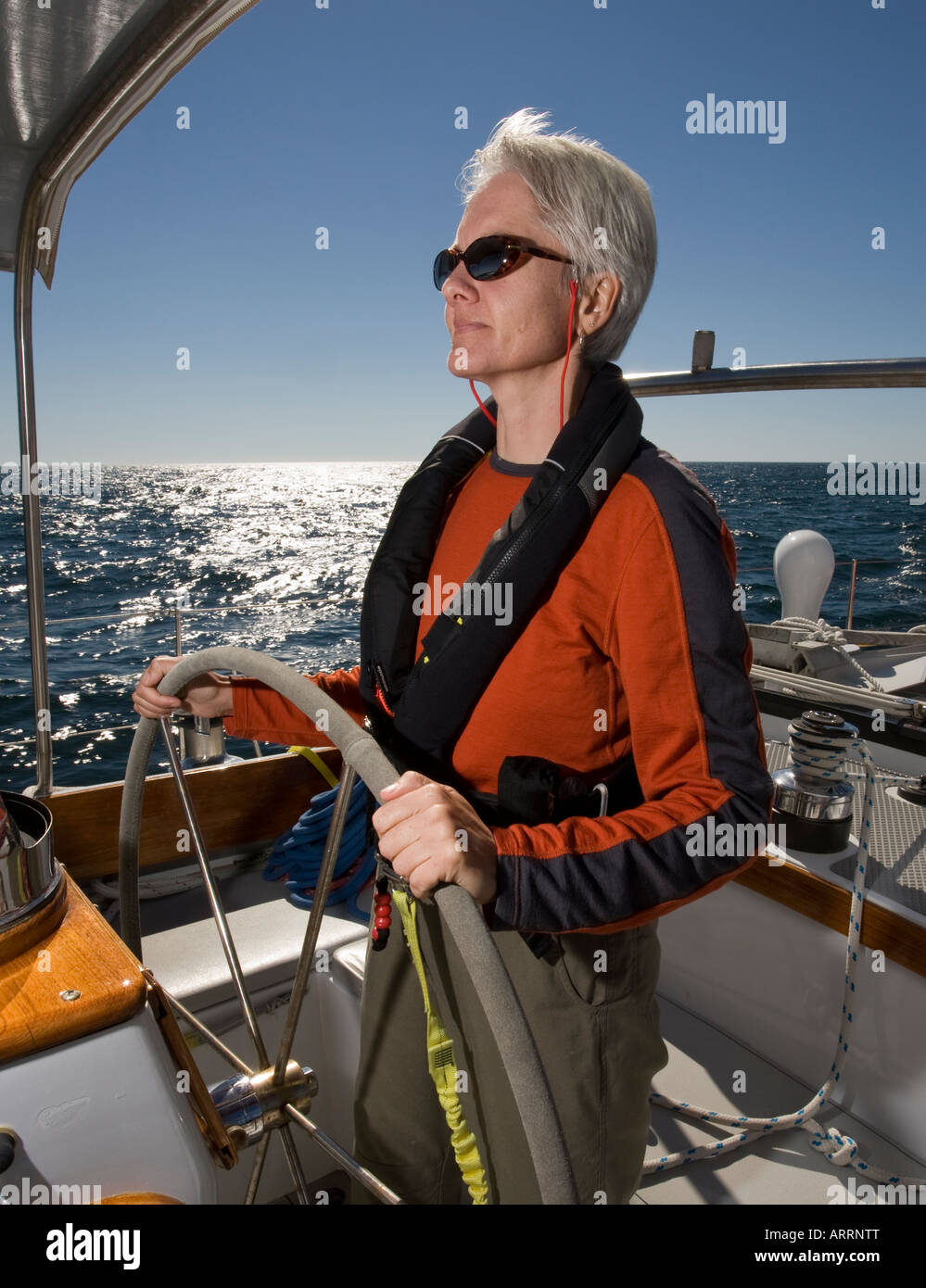 Phyllis Nickel at the helm of sailboat, Morgan's Cloud, during a sunny windy afternoon sail off Jonesport, Maine, USA. Stock Photo