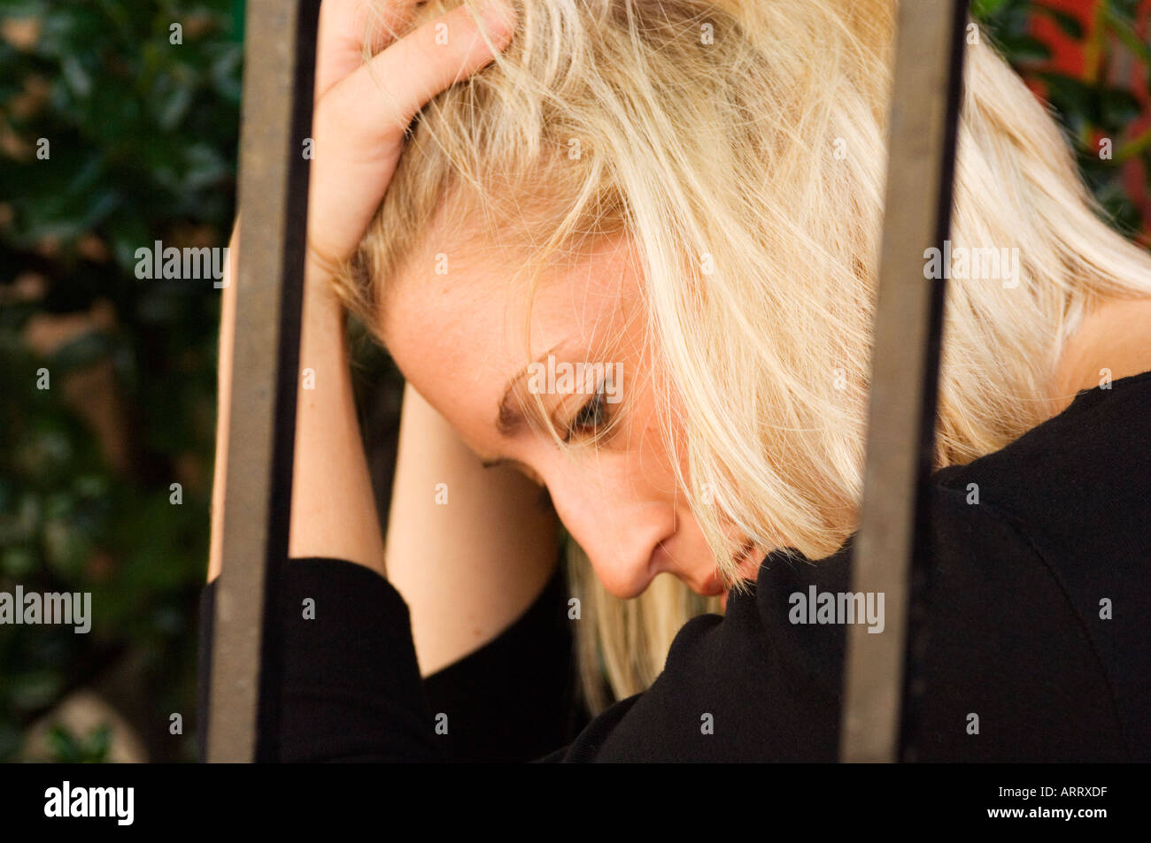Blonde woman sitting dejected behind bars Stock Photo