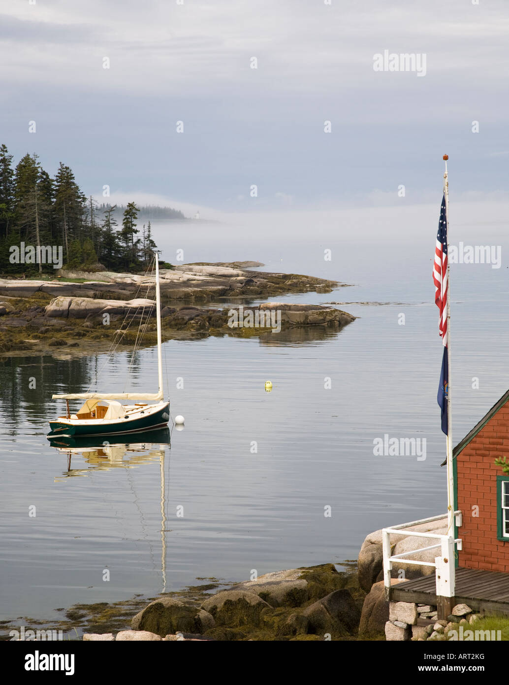 A catboat lies to her mooring in a rockbound cove on a foggy day on Deer Isle, Maine. Stock Photo