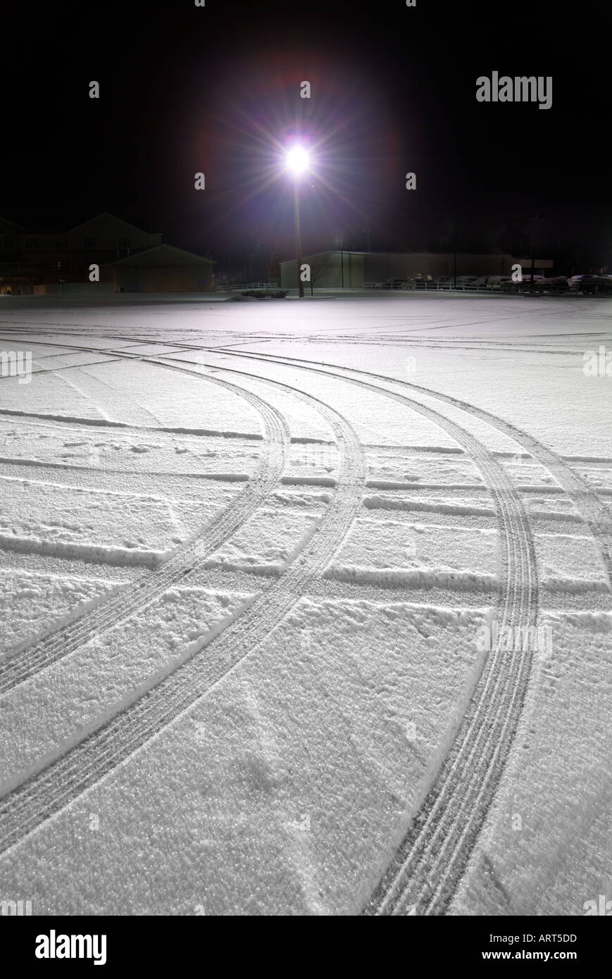 Tire Tracks In Snow At Night, Lone Light In Parking Lot Stock Photo