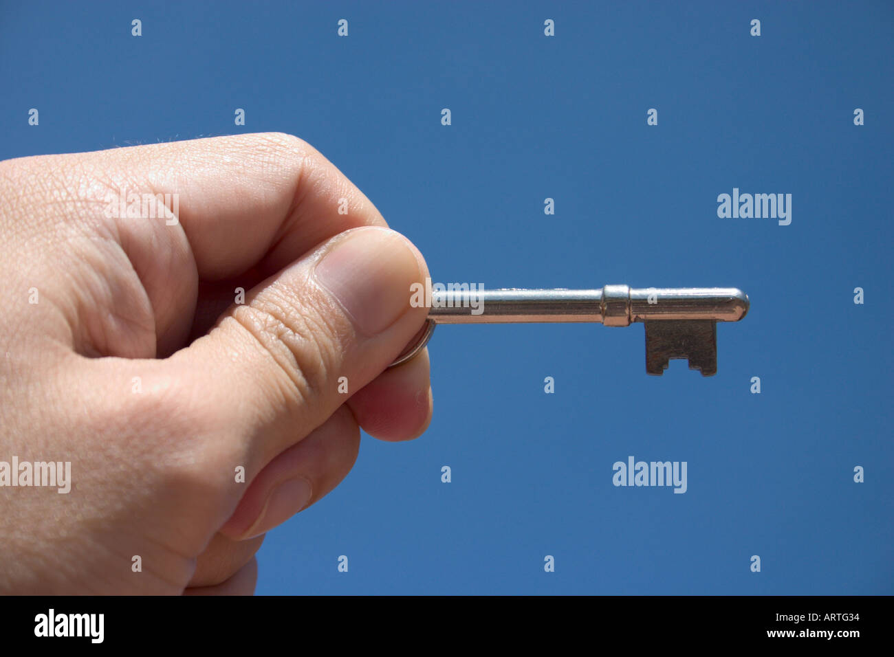 hand holding key against blue sky Stock Photo