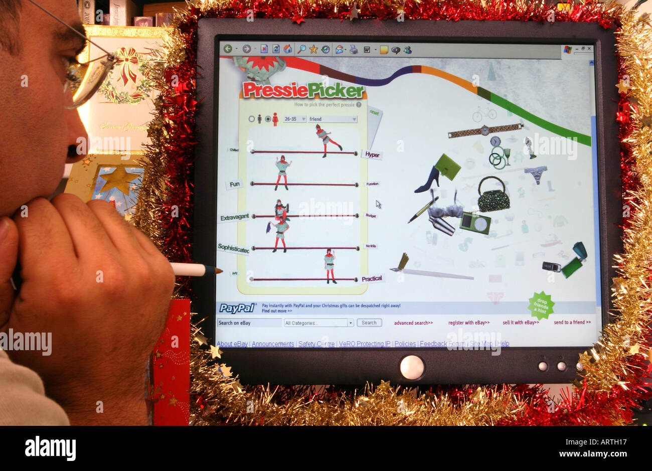 A man at home viewing a Christmas-themed page of the web site ebay on a computer decorated with tinsel. Stock Photo