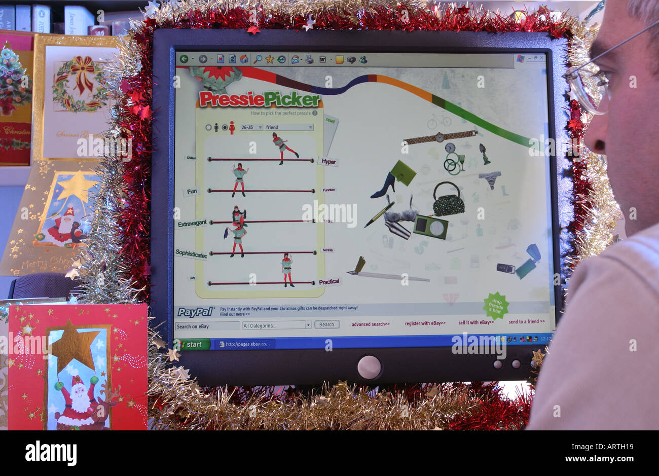 A man at home viewing a Christmas-themed page of the web site ebay on a computer decorated with tinsel. 2005. Stock Photo