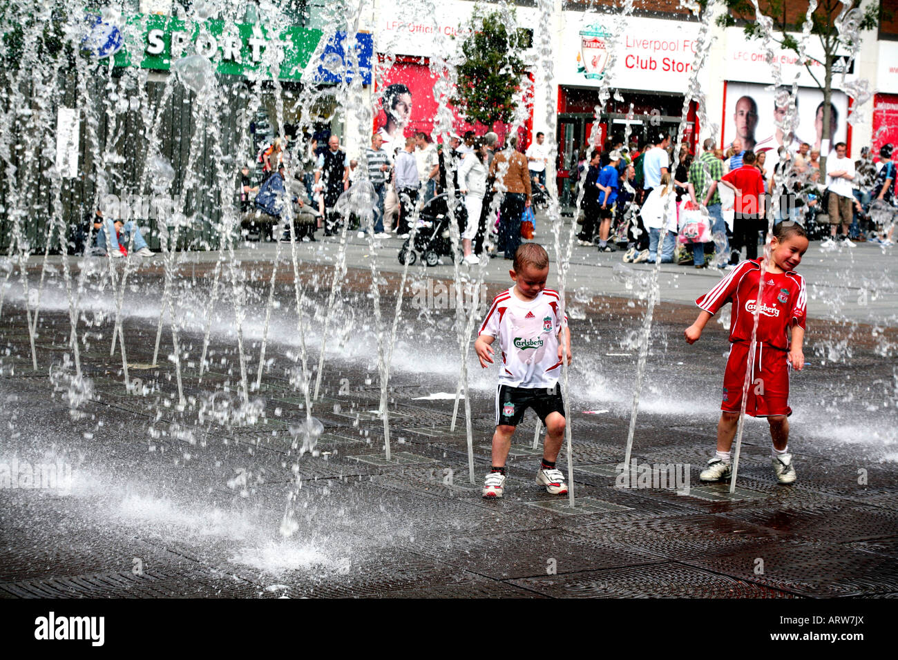 Children in football colours play in fountains in front of Liverpool FC supporters store in Williamson Square Liverpool Stock Photo