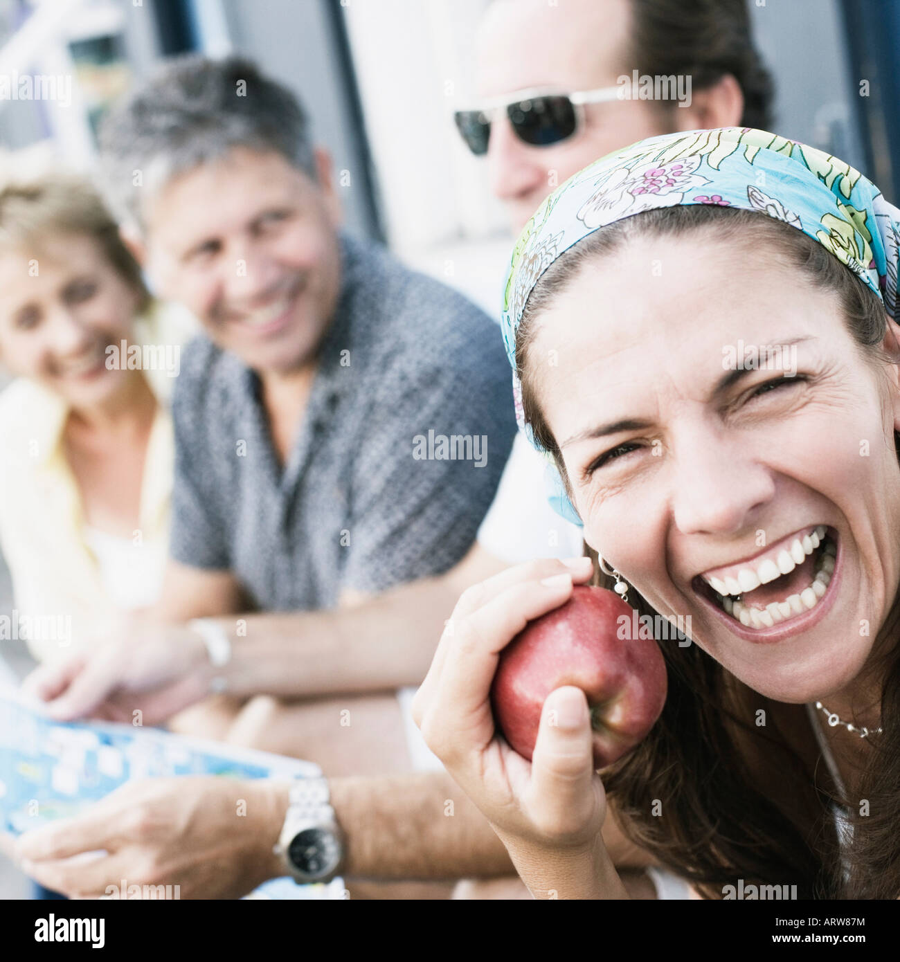 Portrait of a mid adult woman holding an apple with her friends beside her Stock Photo