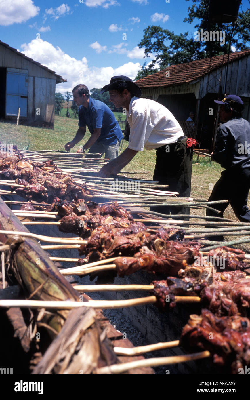 Paraguayan men preparing meat on skewers over a parrilla a barbeque an open fire pit near Trinidad and Jesus Paraguay Stock Photo
