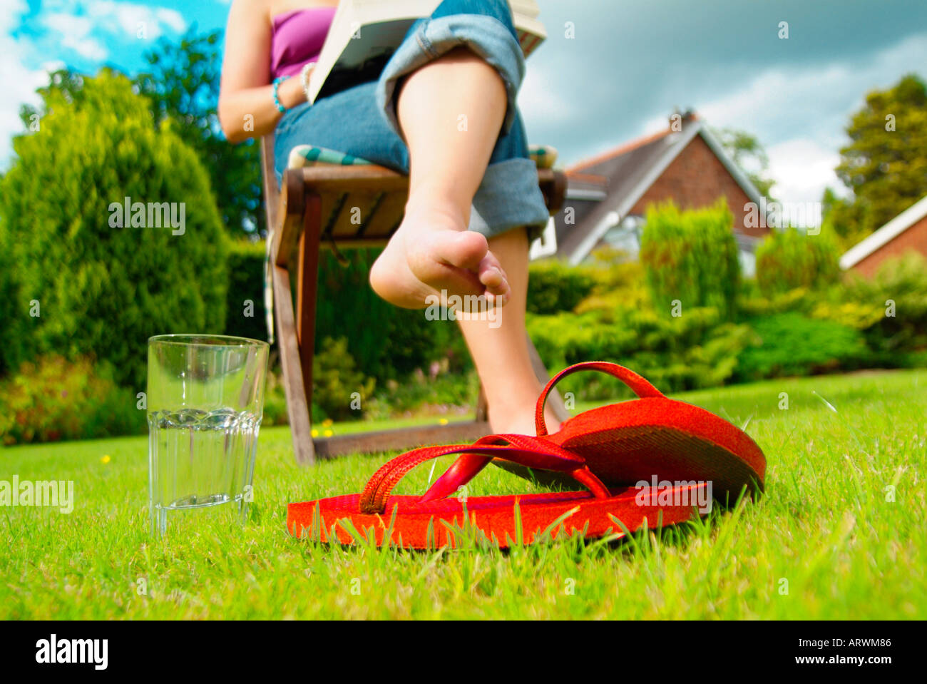 Woman sitting on deck chair in garden with shoes on grass Stock Photo