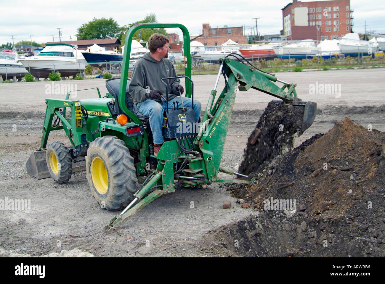 Man Using Backhoe Adult male construction worker uses back hoe to dig a trench to lay ...