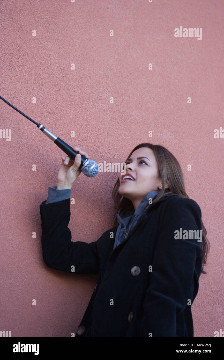 Hispanic woman, twenties, singing into microphone outdoors looking up Stock Photo